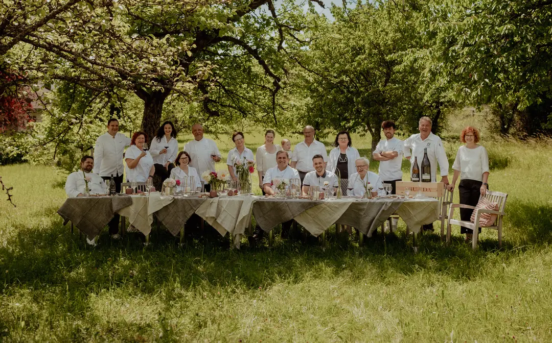 Die acht Schlemmerwirte gemeinsam an einer langen, festlich gedeckten Tafel im Obstgarten
